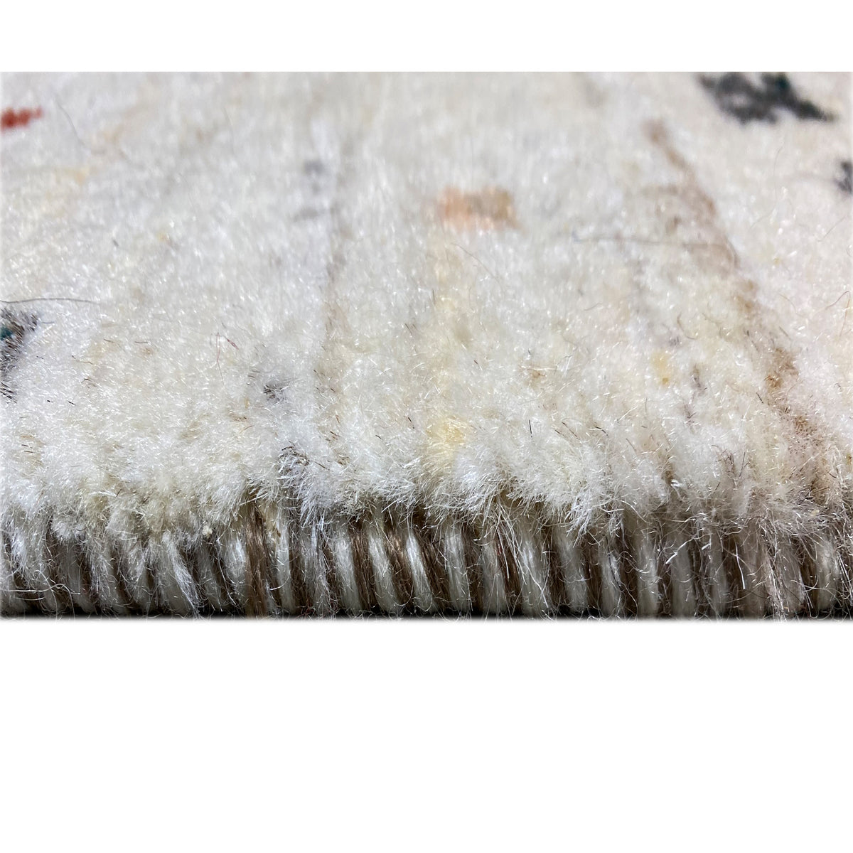 Close-up of the pile of a Gabbeh rug with a soft, light-colored pile and fringed edge.