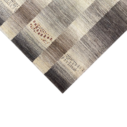 Gabbeh rug corner with patterned blocks in gray and cream, with a small red ornamental element
