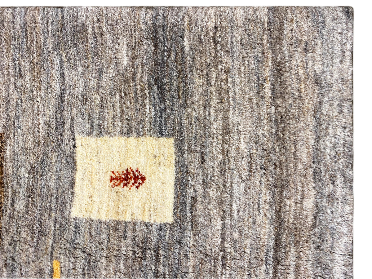 Gabbeh-Teppich Close-up: grauer Flor mit hellem Quadrat und kleinem roten Motiv