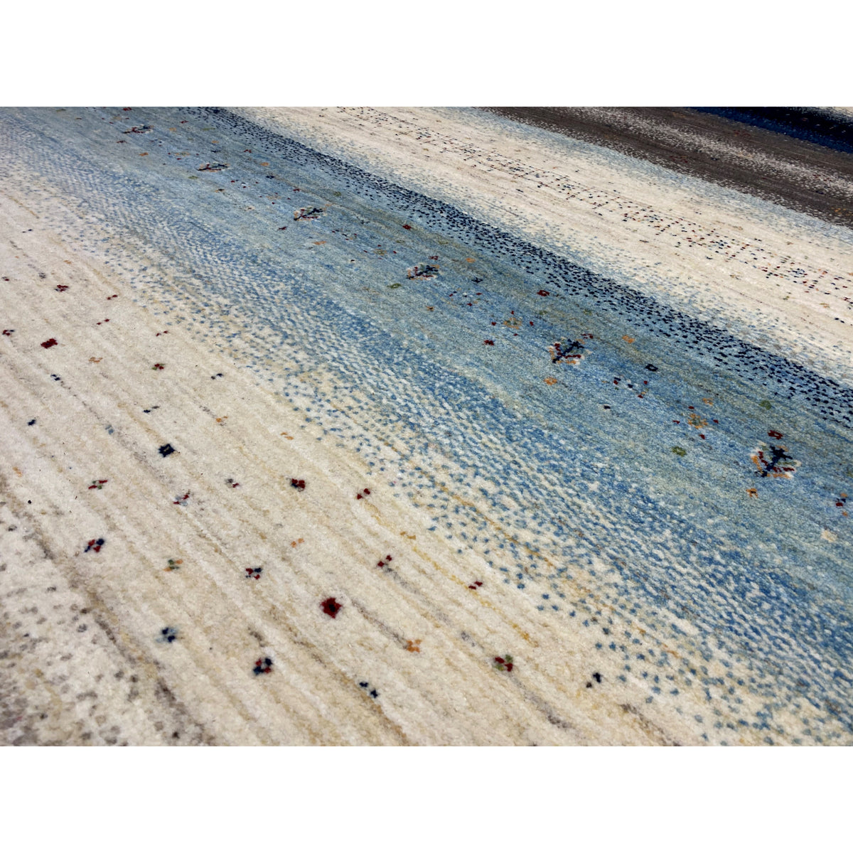 Close-up of a Gabbeh rug: light-colored surface with a blue stripe and fine colored dots