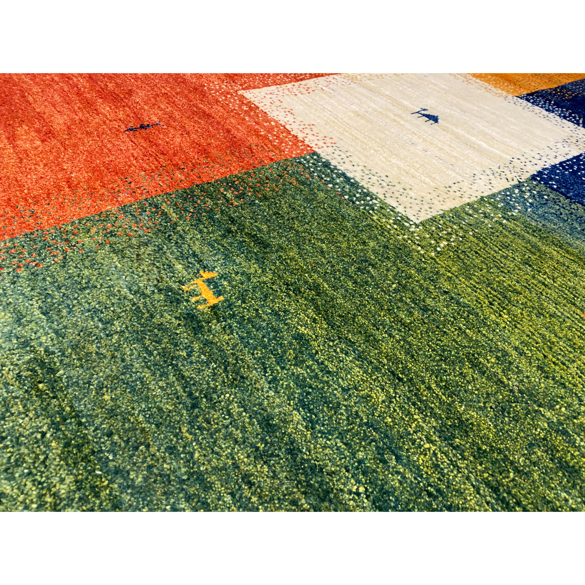 Close-up of a Gabbeh rug: textured green pile with colorful motifs and a white corner section