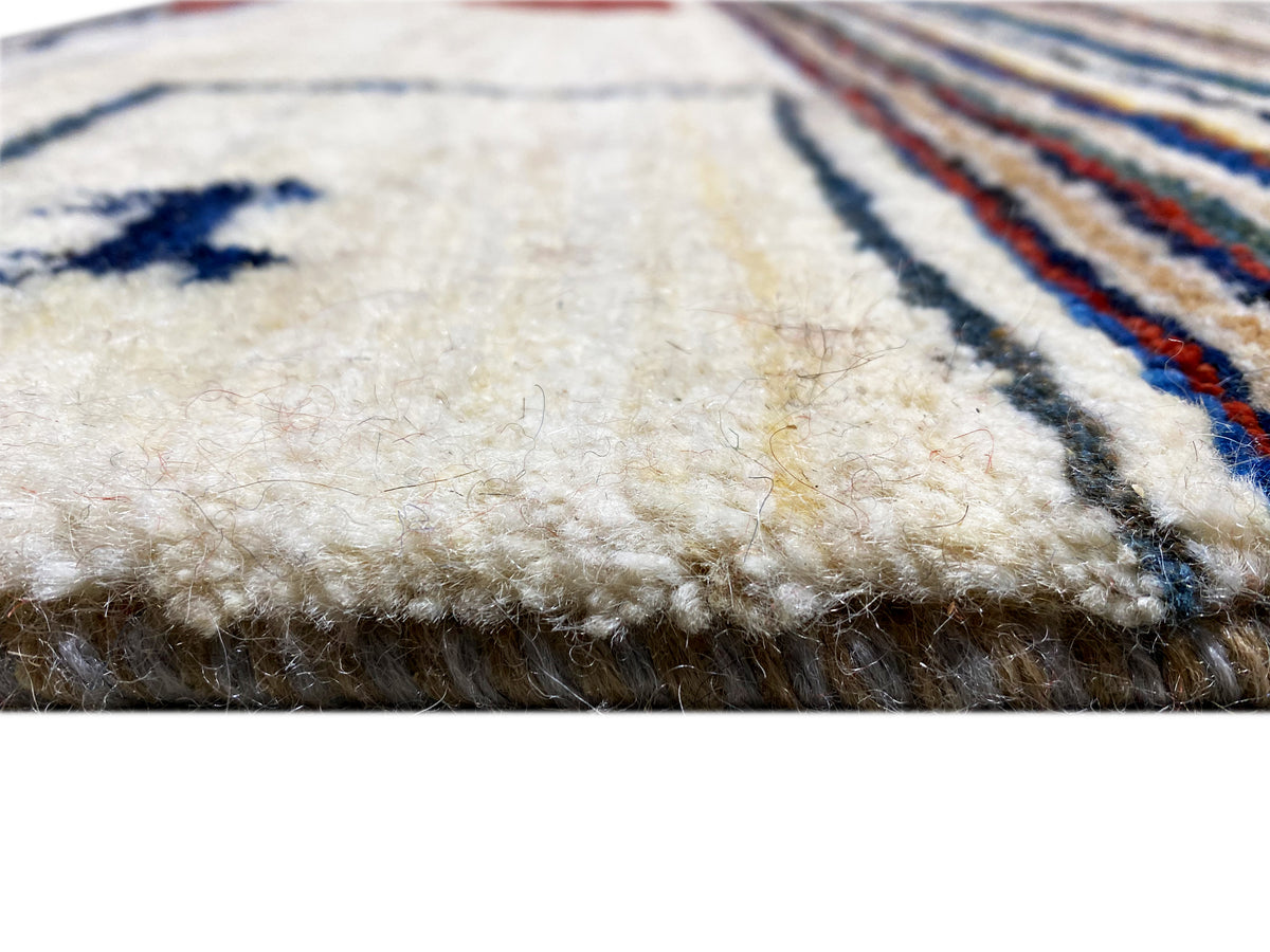 Gabbeh-Teppich Detail am Rand: raue Florstruktur auf cremefarbener Fläche mit Blau-Element.