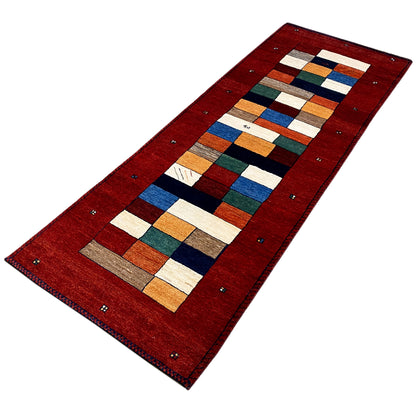 Red Gabbeh runner rug viewed at an angle, rectangular pattern and surrounding border