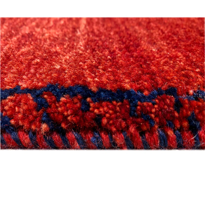 Close-up of a Gabbeh rug runner: dense red pile with a dark blue edge border
