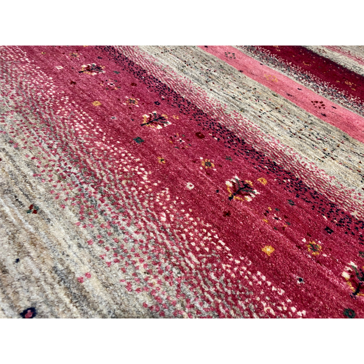 Close-up of a Gabbeh rug: red and pink striped pattern with beige and black speckles