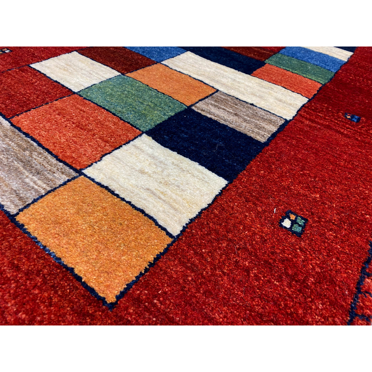 Close-up: Red rug with contrasting patchwork sections in orange, blue, green, and white