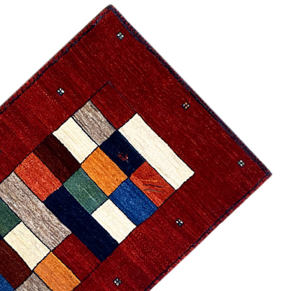 Corner of a red table runner with a geometric pattern of white, blue, green, and orange squares