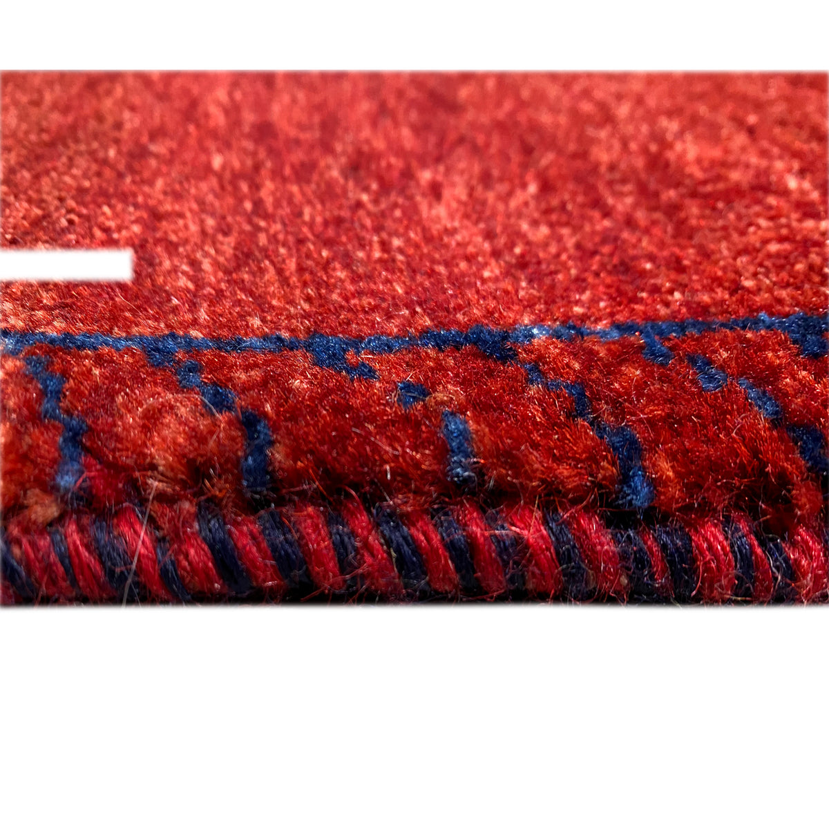 Close-up of a Gabbeh rug runner: red pile with blue decorative stitching and fringes