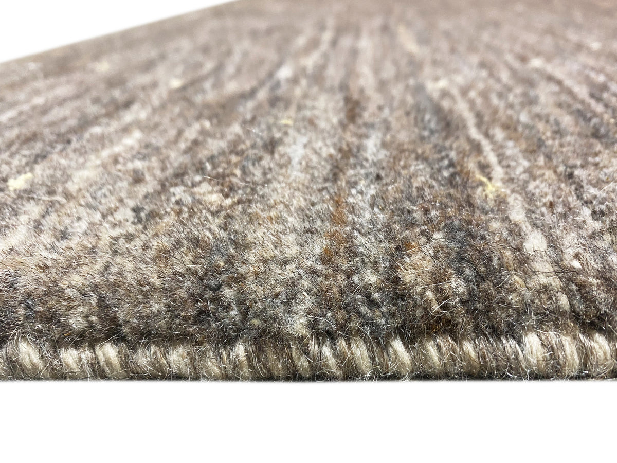 Carpet edge with a dense pile border; heathered fibers in gray, beige, and light sections.