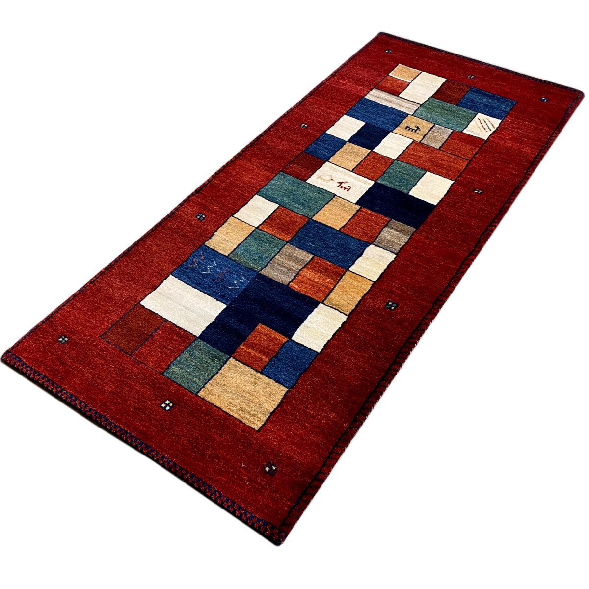 Gabbeh runner rug viewed diagonally from the front: red grid pattern with white, blue, and green blocks.