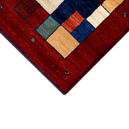 Corner of the red Gabbeh runner rug with a dark border and small embellishments