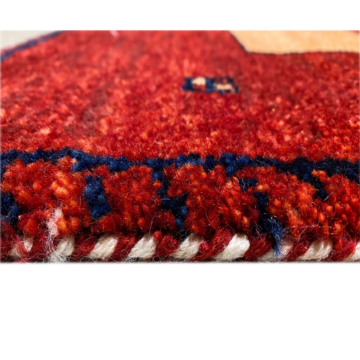 Close-up: red and blue carpet pile with a dark border and multicolored pattern elements.