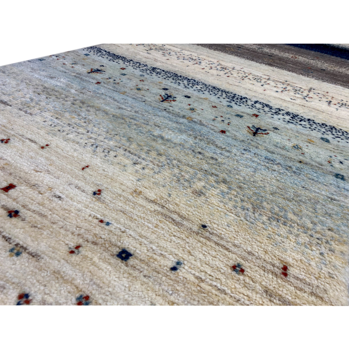 Close-up of a Gabbeh rug: light-colored yarns, a light blue gradient, and small colorful pattern dots
