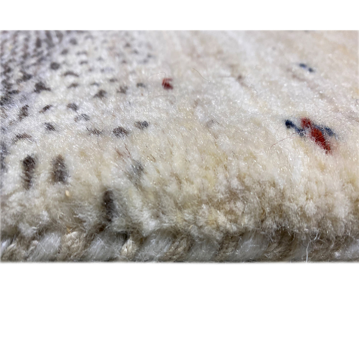 Close-up of a Gabbeh rug runner, dense light-colored pile with occasional colorful embroidered patterns