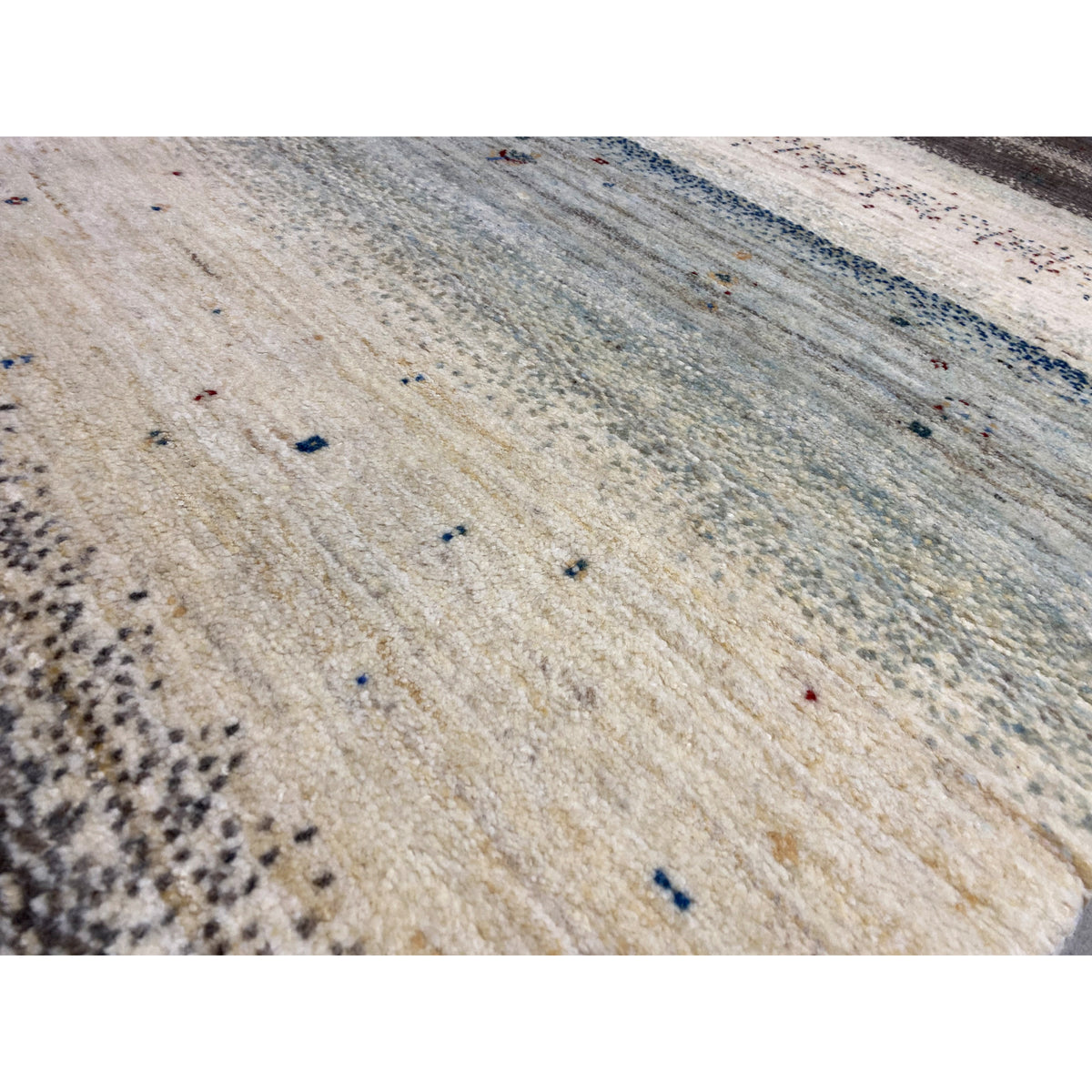 Close-up of a Gabbeh rug: light beige texture with blue and black dot accents