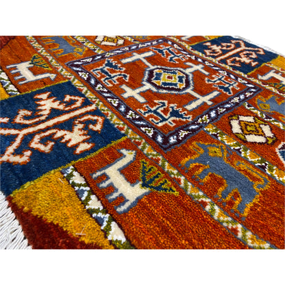 Close-up of a Gabbeh rug: woven patterns in blue, orange, and yellow with fringes.