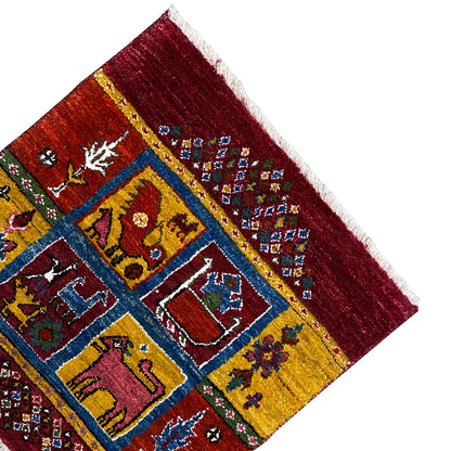 Corner of a Gabbeh rug with a burgundy border, yellow-and-blue geometric pattern, and white fringes