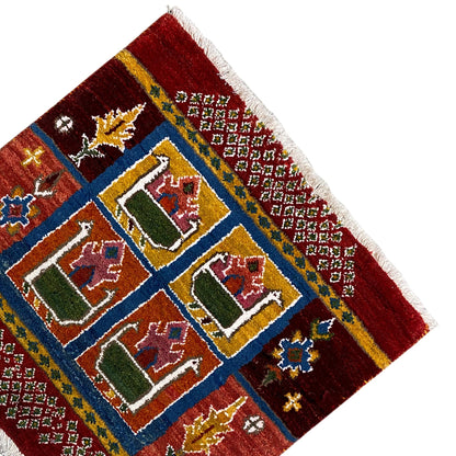 Red Gabbeh rug with a diagonal perspective, blue-outlined house motifs, colorful details, fringes