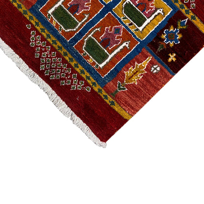 Red Gabbeh rug, blue-and-yellow band with squares, house motifs, white fringe along the edges
