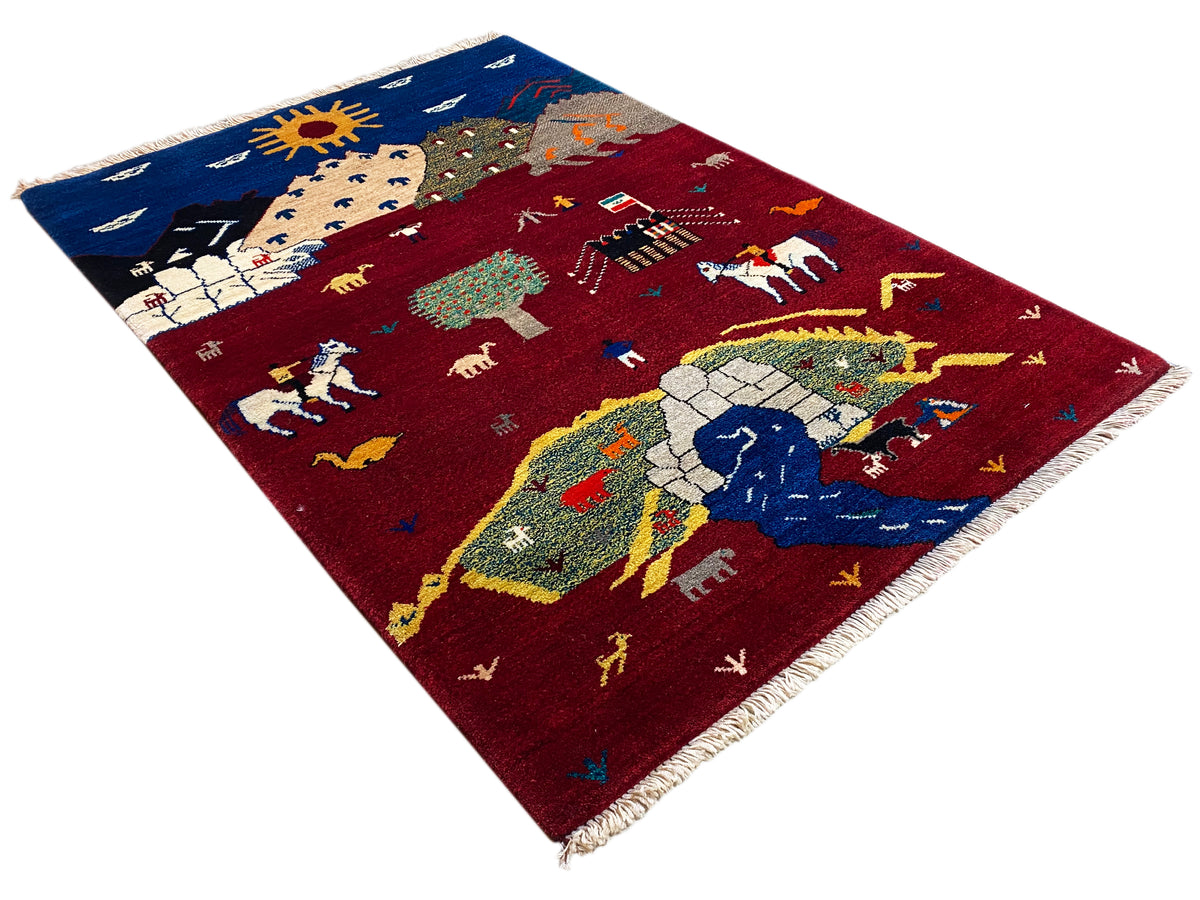Gabbeh Luri rug at an angle, red pattern with sun, riders and animals, fringes