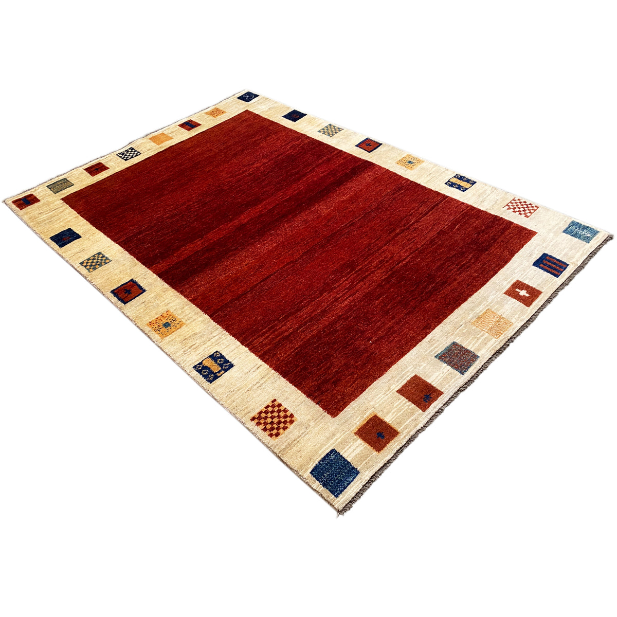 Gabbeh rug at a three-quarter angle: red center, cream-colored border with symbols