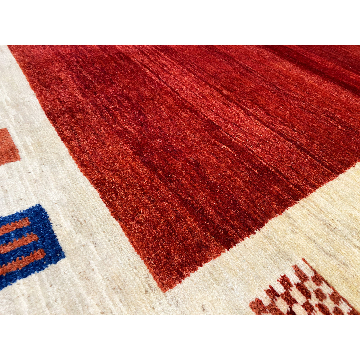 Gabbeh rug detail: reddish-brown pile design, cream-colored border with blue patterns