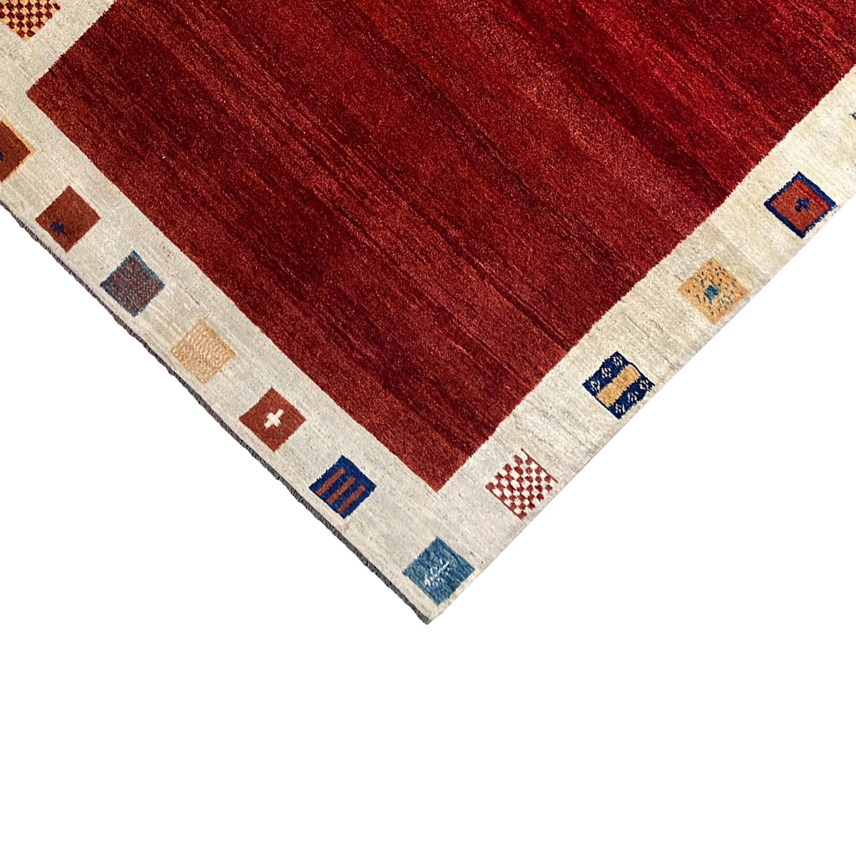 Close-up of the corner of a Gabbeh rug: dark red field, cream-colored border with small symbols