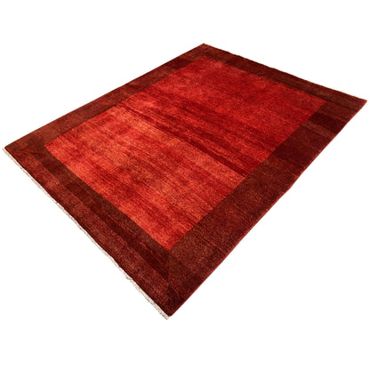 Gabbeh rug with a red central section and brown border trim, diagonal view