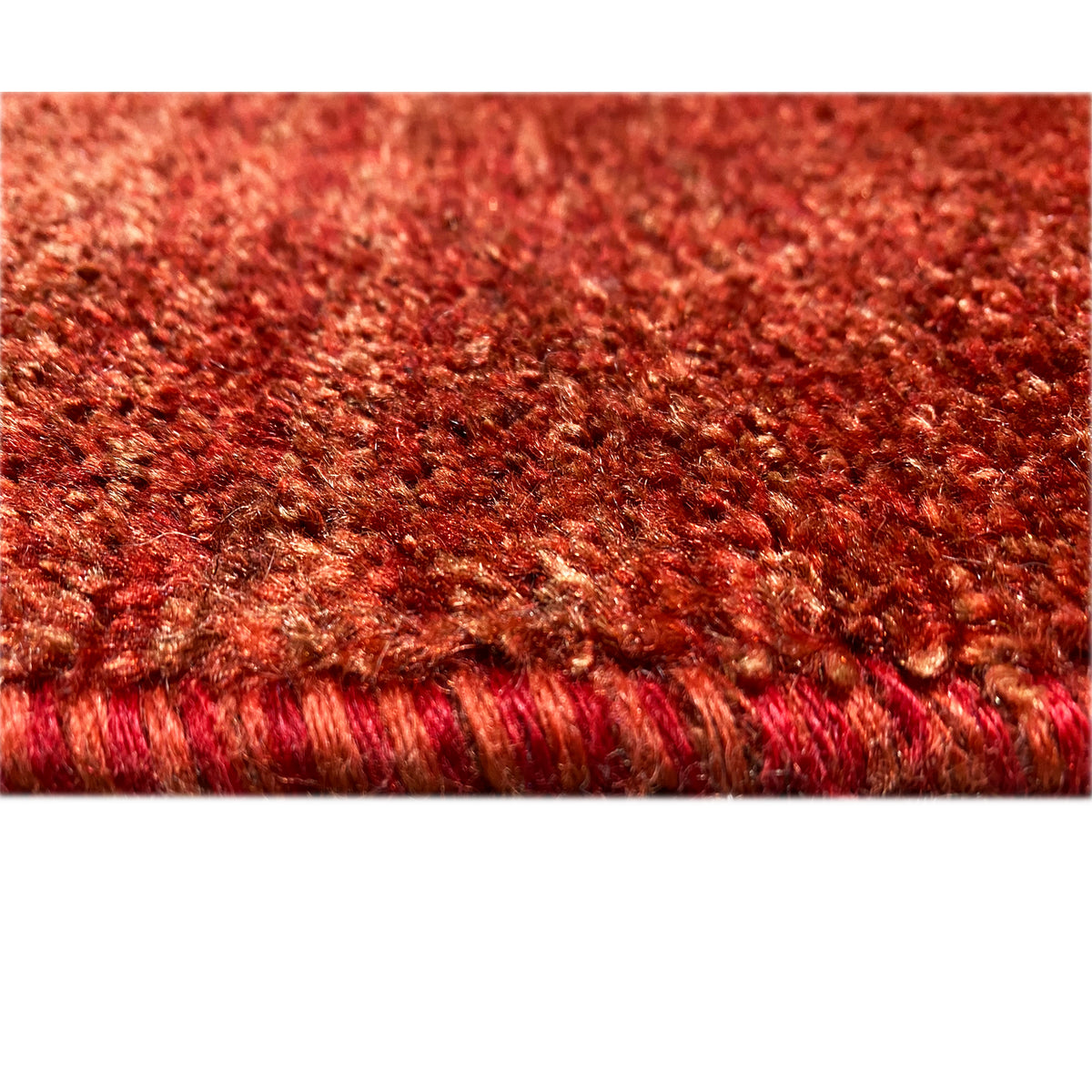 Close-up of a Gabbeh rug at the edge: dense red pile with a mottled pattern