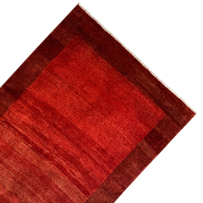 Gabbeh rug with a red central section and brown border, corner view