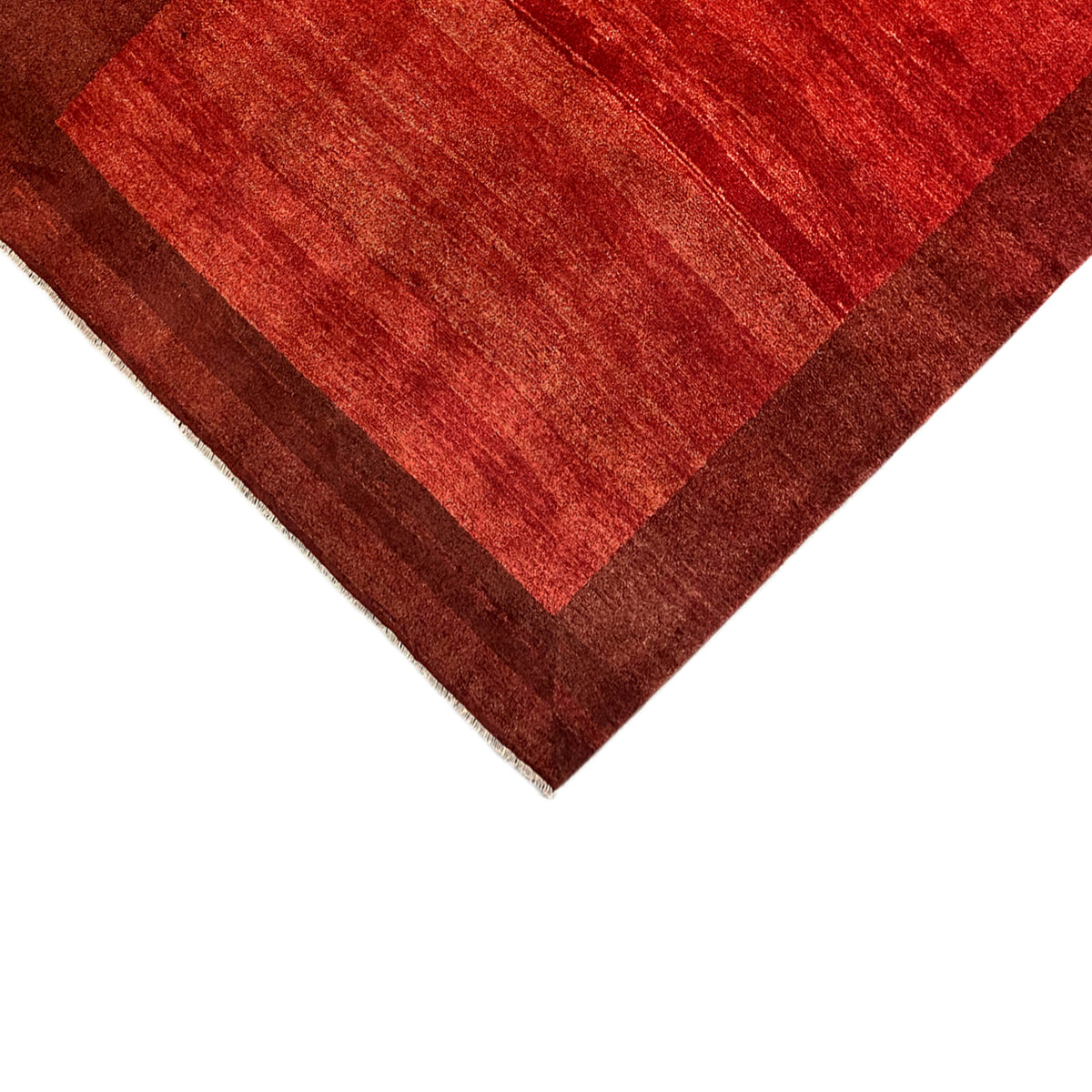 Corner of the Gabbeh rug with a reddish-brown striped pattern and brown border trim