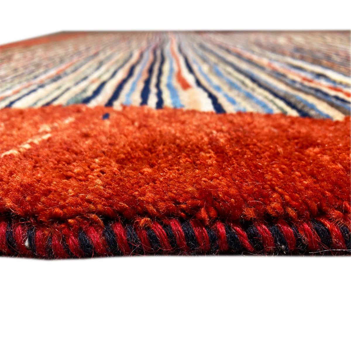 Close-up of a carpet edge: reddish pile with a dark fringed border, stripes in the background
