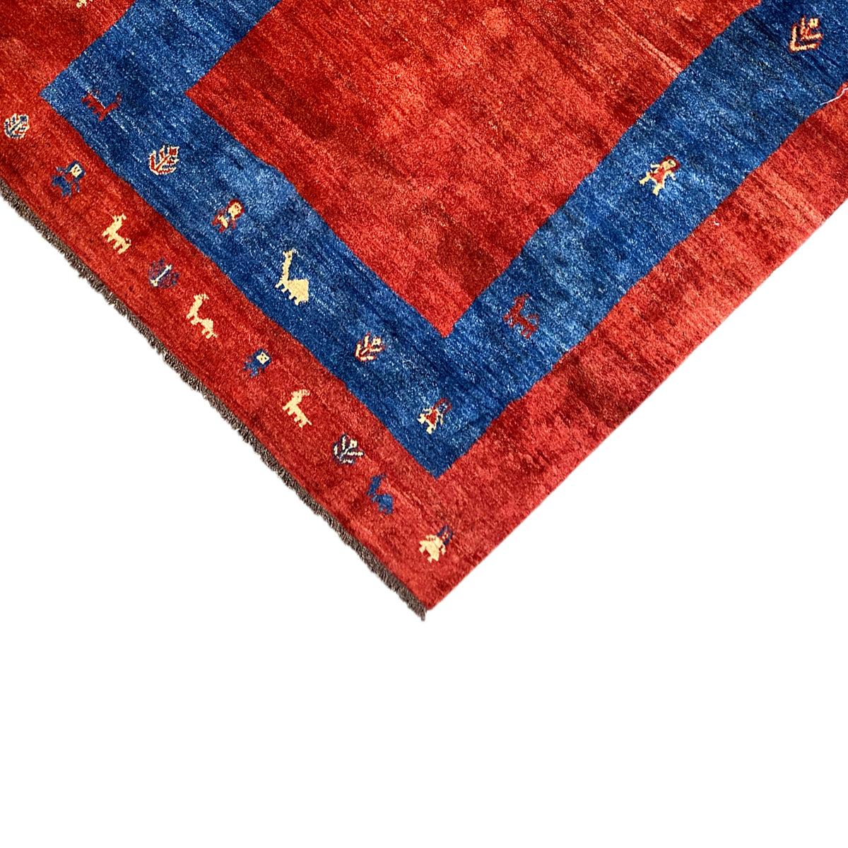 Close-up of rug edge: red border, blue patterned field, and finely hemmed fringe finish