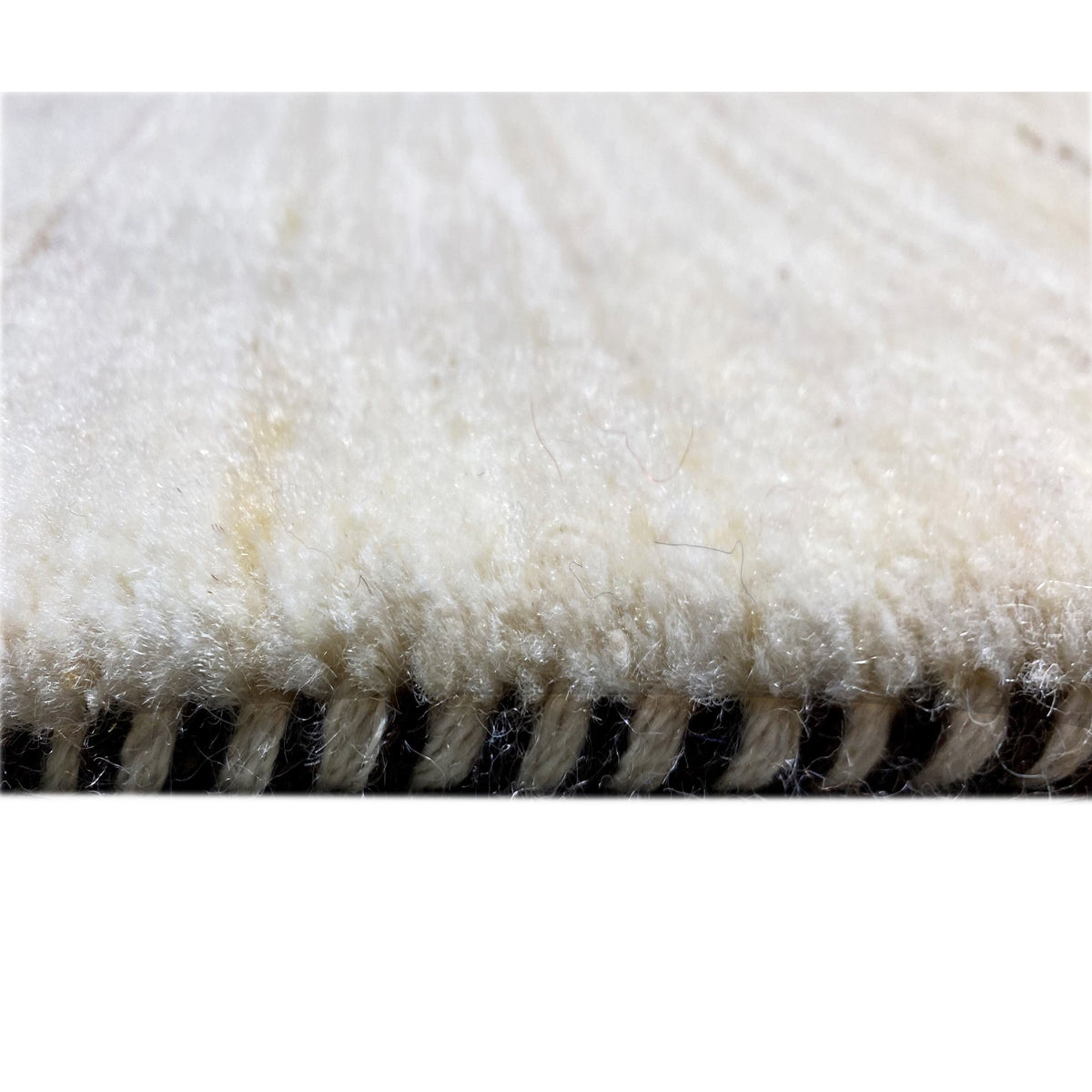 Gabbeh rug detail: dense beige pile with a jagged edge along the side