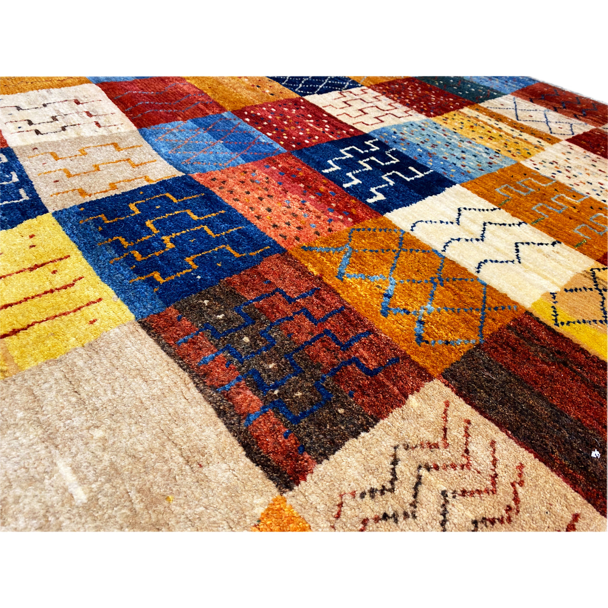 Close-up view of a Gabbeh rug: colorful patchwork blocks with embossed details and zigzag patterns, textile texture