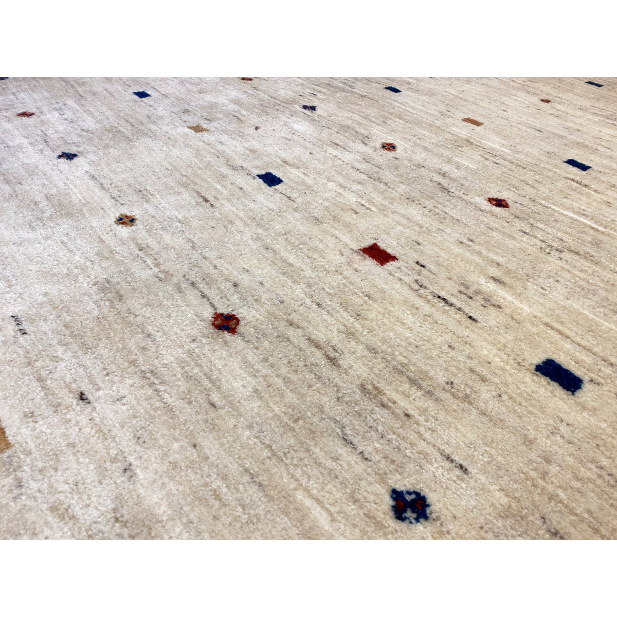 Close-up of a Gabbeh rug: light beige pile with red and blue patterned dots