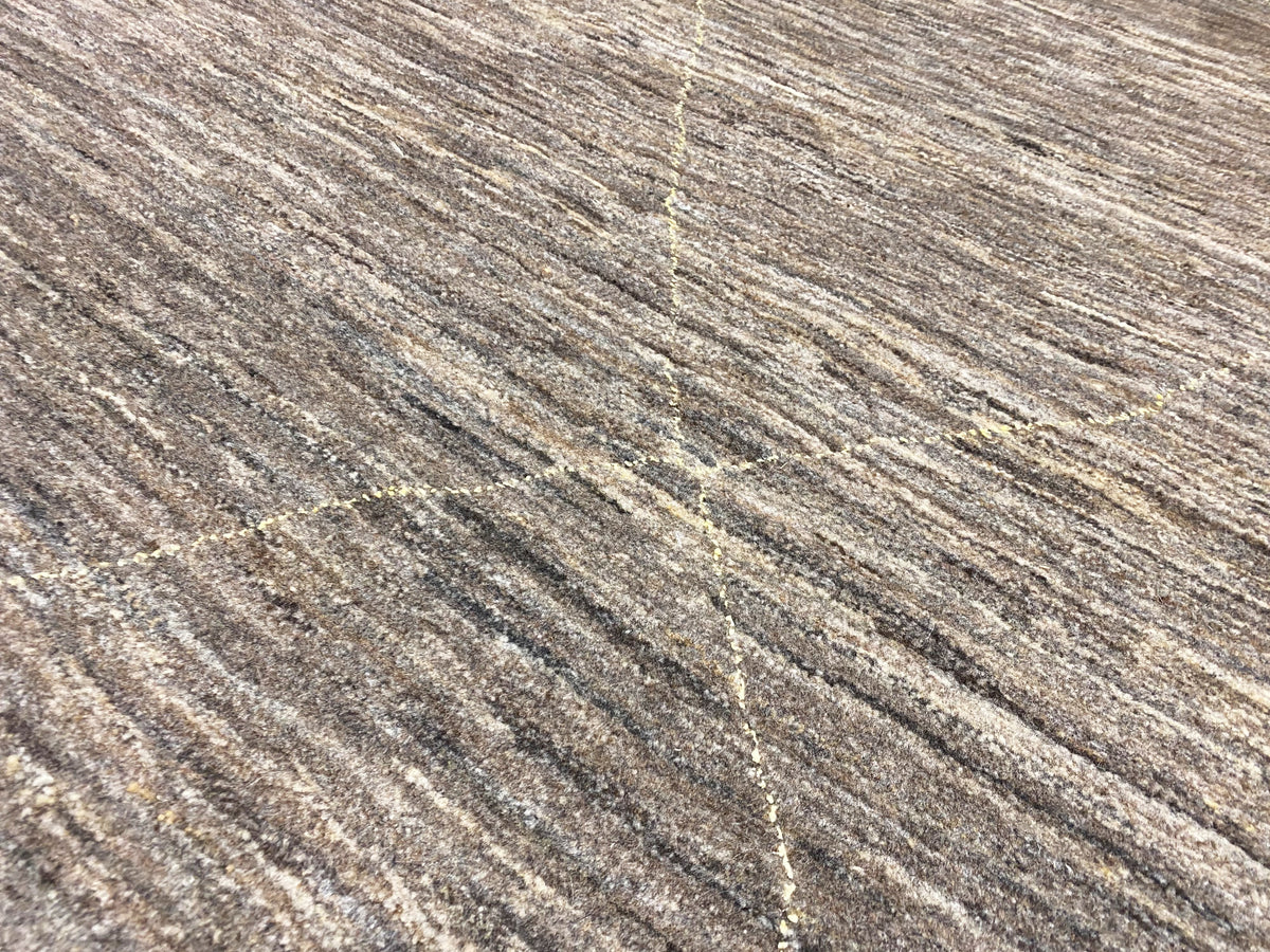Nahaufnahme: melierte Teppichoberfläche in Grau-Beige mit goldfarbenen Fadenakzenten und Linien.