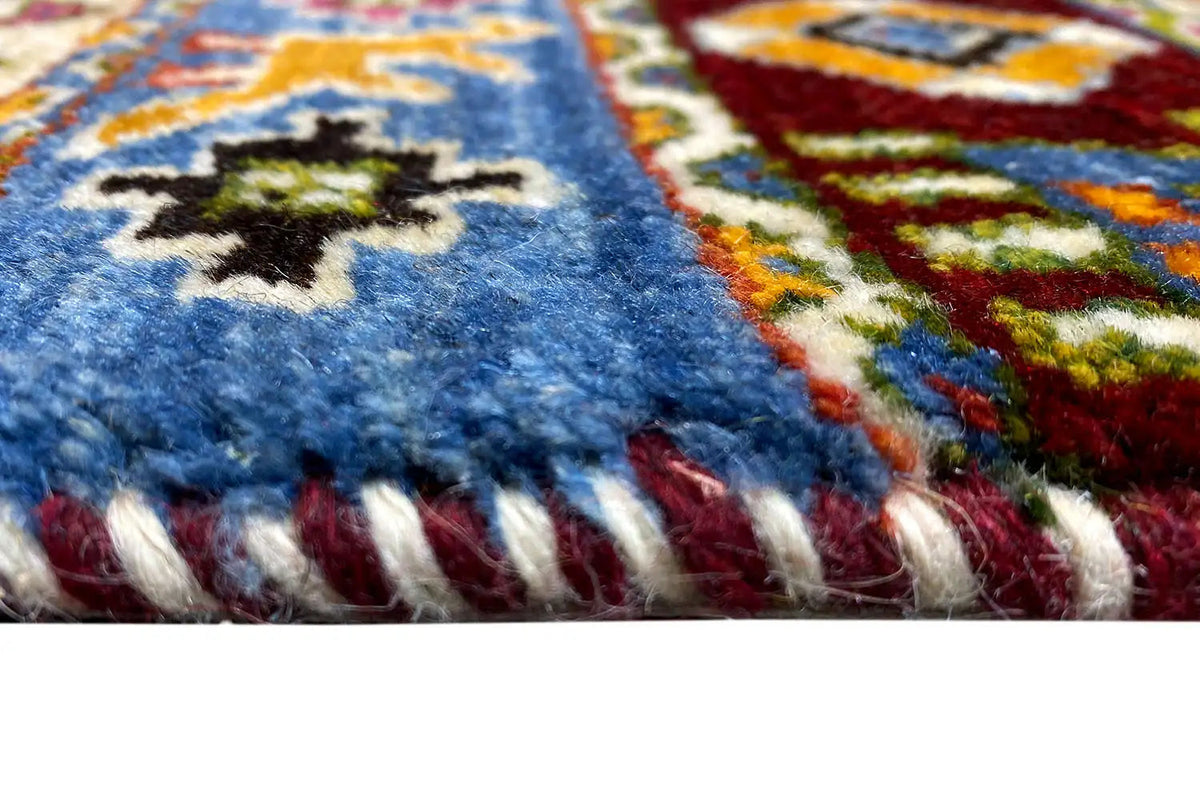 Close-up of a Gabbeh rug with a blue pile, colorful accents, and a fringed edge.