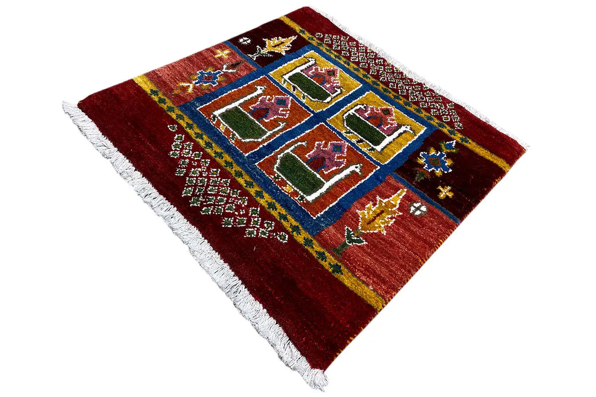 Red Gabbeh rug with a blue square border, colorful house motifs, and a white fringed edge