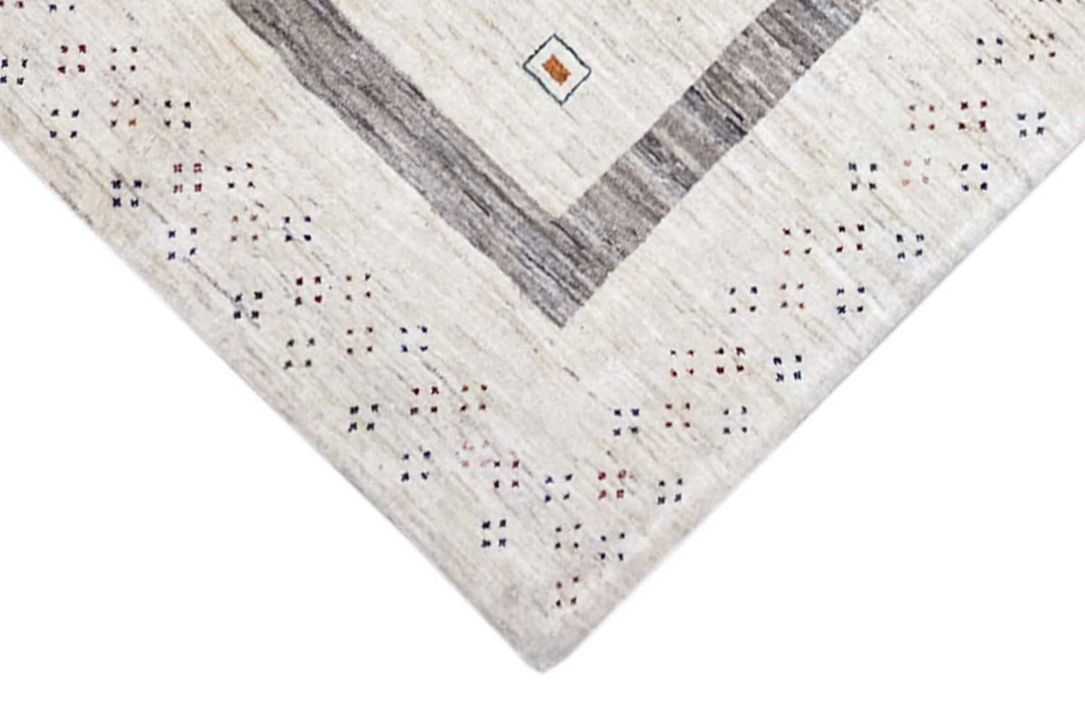 Corner of a beige Gabbeh rug with gray stripes and a small pattern along the edge