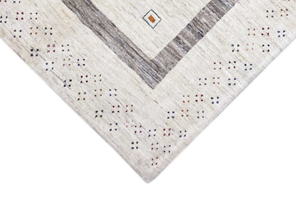 Corner of a beige Gabbeh rug with gray stripes and a small pattern along the edge