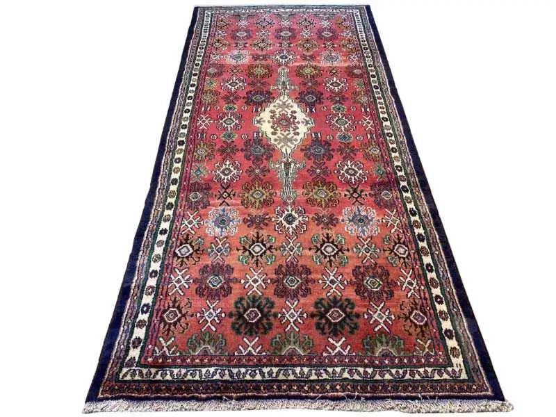 Oriental rug, red with colorful ornaments and a wide blue-and-white border, shown at an angle