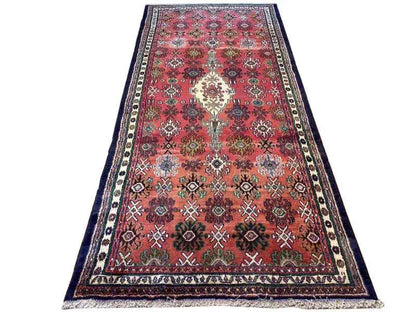 Oriental rug, red with colorful ornaments and a wide blue-and-white border, shown at an angle