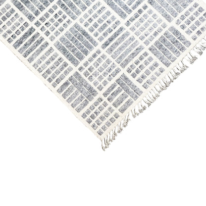 Corner view of a gray-and-white rug with a geometric grid and fringes
