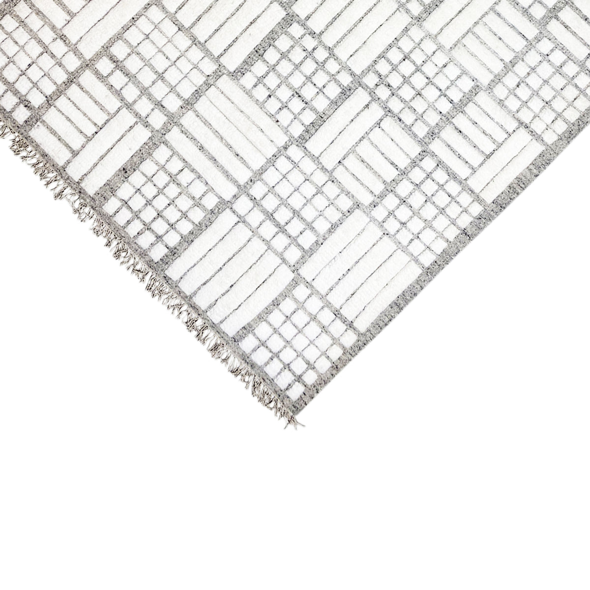 Corner of a Berber rug with a white and gray diamond grid, fringed