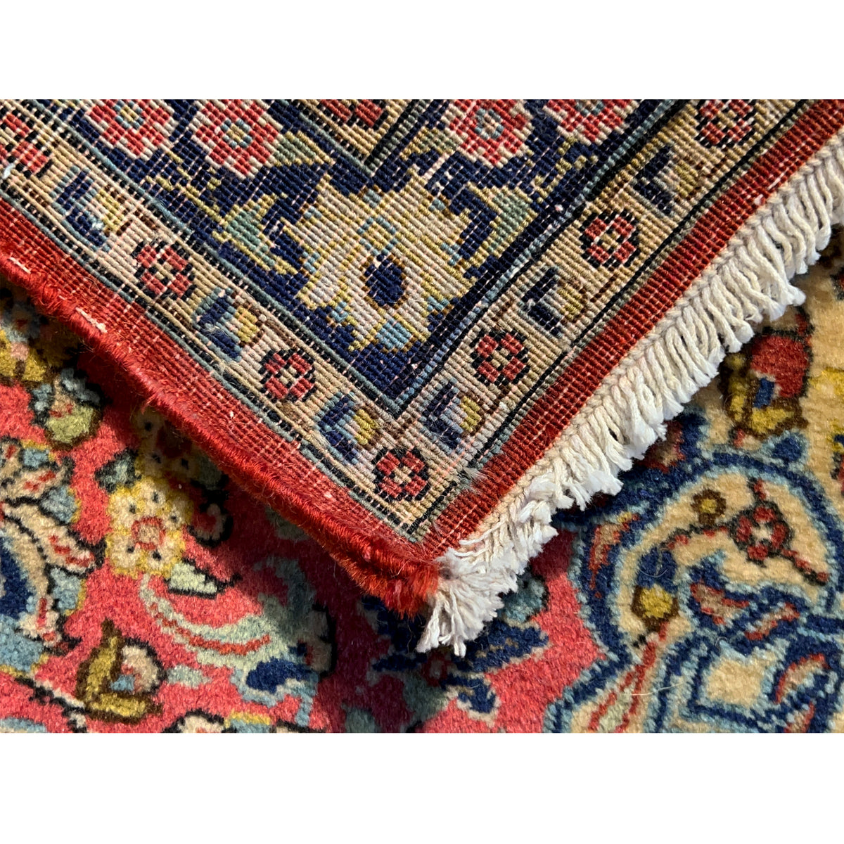 Rug corner with red edging, a blue/yellow pattern, and white fringes