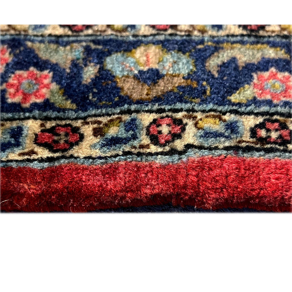 Close-up of a rug with a blue border, colorful medallions, and red pile