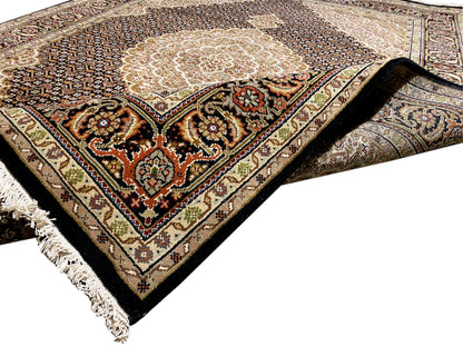 Teppich in Ecke: beiges Medaillon, dunkles Feld mit Ornamenten, Zierbordüre und Fransen.