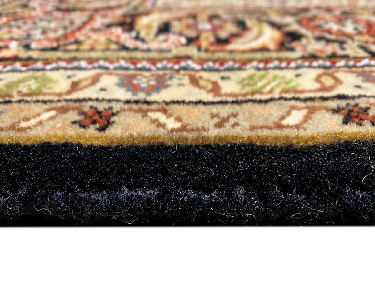 Nahaufnahme der Teppichkante mit Fransen und dunklem Flor, darunter Muster in Beige und Braun