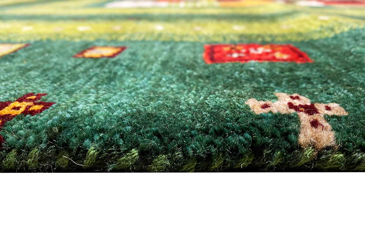 Close-up of a Gabbeh Lori rug: green pile with colorful pattern elements